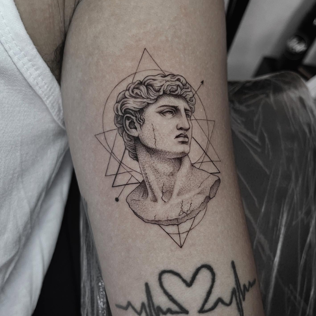 Black ink bust tattoo with geometric shapes on arm.