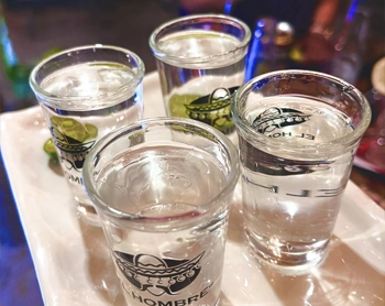 Four tequila shots served on a white tray at a bar.